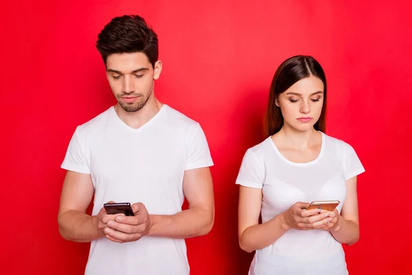 Foto van ernstige geconcentreerde echtgenoten op zoek naar in hun telefoons chatten met elkaar zonder emoties op het gezicht in witte t-shirt geïsoleerde levendige kleur achtergrond — Stockfoto
