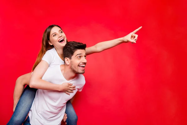 Photo of pretty sweet positive nice cheerful couple boyfriend girlfriend with her showing the way and him carrying her in jeans denim white t-shirt pointing isolated bright color background — Stock Photo, Image