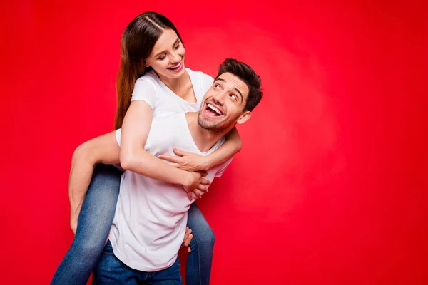 Foto de alegre positivo bonita pareja de cónyuges con chico llevando a cuestas chica y su montar su espalda abrazándose en jeans vaqueros camiseta blanca aislado color vivo fondo —  Fotos de Stock