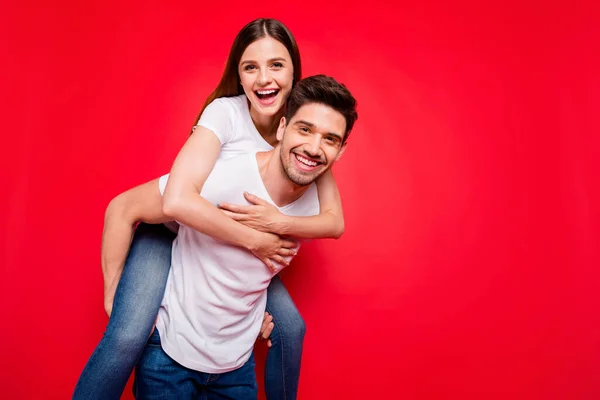 Photo of cheerful positive pretty couple of two people piggyback girl hugging riding guy in jeans denim white t-shirt carrying near empty space isolated vivid color background — Stock Photo, Image