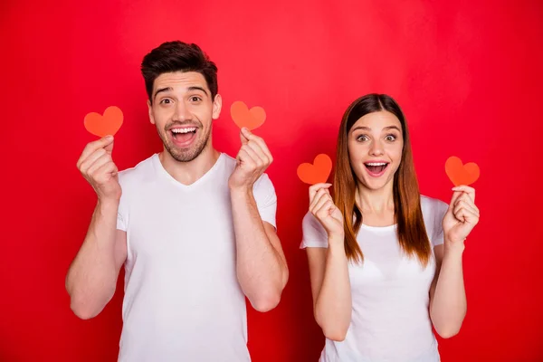 Photo of cheerful positive nice cute charming pretty couple boyfriend girlfriend smiling excited about receiving postcards showing small heart shapes isolated in white t-shirt vivid color background — Stock Photo, Image
