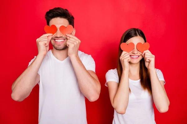 Foto de alegre positivo muito bom casal de pessoas amorosas cobrindo seus olhos com pequenos corações cartões postais sorrindo dente isolado fundo de cor vívida vestindo t-shirt branca — Fotografia de Stock