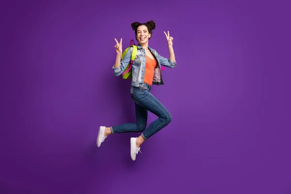 Full length profile photo of funny student lady jumping high showing v-sign symbols wear green bag casual denim stylish outfit isolated purple color background — Stock Photo, Image