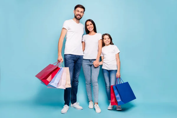 Повна довжина фотографії позитивних трьох людей мама тато школярка залежний від коричневого волосся магазин тримає руку обіймає носіння білої футболки джинсові кросівки ізольовані на синьому кольорі — стокове фото