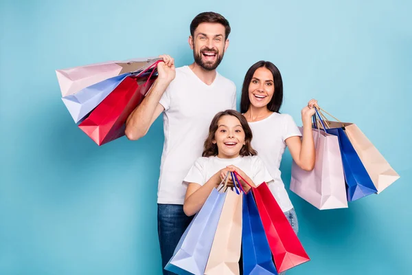 Retrato de emocionado positivo alegre tres personas mamá papá colegial con pelo marrón tienda centro celebrar bolsas usar blanco camiseta vaqueros aislados sobre fondo de color azul — Foto de Stock