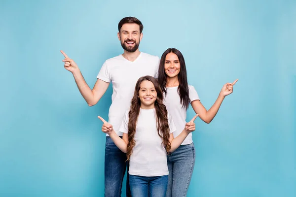 Retrato de positivo alegre tres personas promotores apuntan en el espacio de copia recomiendan ropa de ventas blanco camiseta vaqueros aislados sobre fondo de color azul —  Fotos de Stock