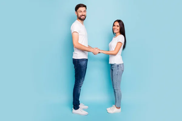 Full Size Profil Seite Foto von ehrlich zufrieden Paar halten Hand haben Datum freie Zeit tragen weißes T-Shirt Denim Jeans Turnschuhe lässigen Stil isoliert über blauer Farbe Hintergrund — Stockfoto