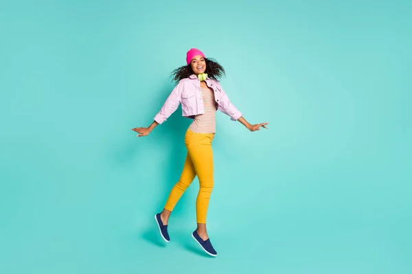 Longitud completa tamaño del cuerpo perfil lateral foto de alegre positivo agradable chica encantadora bailando saltar usando pantalones amarillos en camiseta a rayas aislado sobre fondo de color verde azulado —  Fotos de Stock