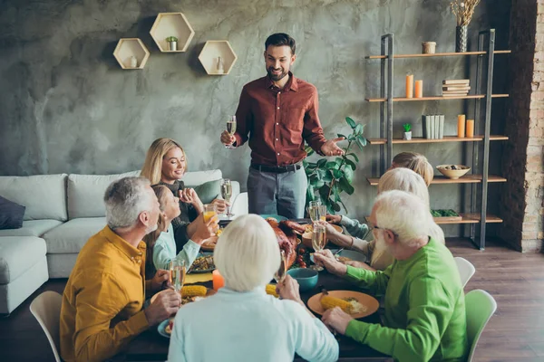 Velká šťastná rodina shromáždit party oslavit Den díkůvzdání sedět stůl těšit pečené kuřecí jídlo muž stojí držet šampaňské skleněné toast na malé děti dospělé generace v domě — Stock fotografie