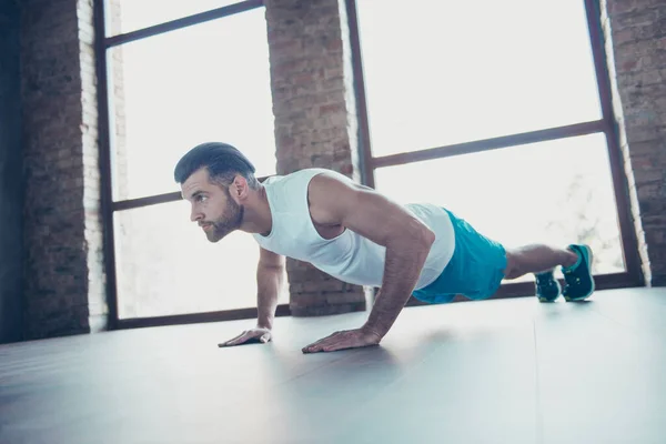 Φωτογραφία προφίλ του macho sportsman τύπος κάνει push ups σανίδα χέρια γέρνει το πάτωμα καθορίζεται εκπαιδευτής αθλητικά ρούχα δεξαμενή-top σορτς sneakers κατάρτισης σπίτι παράθυρα στούντιο σε εσωτερικούς χώρους — Φωτογραφία Αρχείου