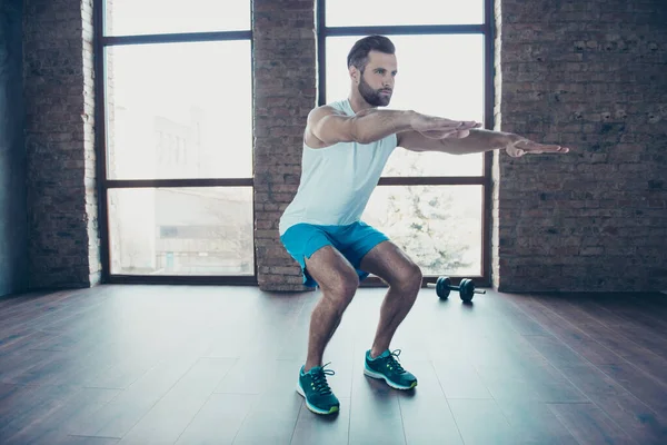 Full length photo of handsome trainer guy doing static squats concentrated sportswear tank-top shorts sneakers training home studio near windows indoors — Stock Photo, Image