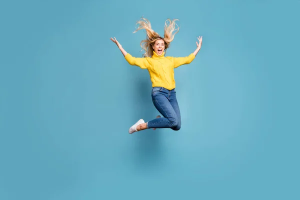 Full body foto van gekke dame springen hoog genieten warme herfst wind kapsel vliegen vrolijk persoon dragen gebreide gele trui jeans geïsoleerde blauwe kleur achtergrond — Stockfoto
