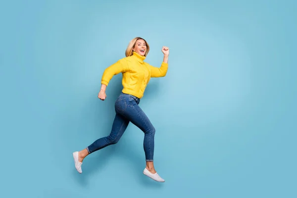 In voller Länge Profilfoto von verrückten Dame springen hoch rauschenden Einkaufszentrum schwarz Freitag Verkauf tragen gestrickte gelbe Pullover Jeans isoliert blaue Farbe Hintergrund — Stockfoto