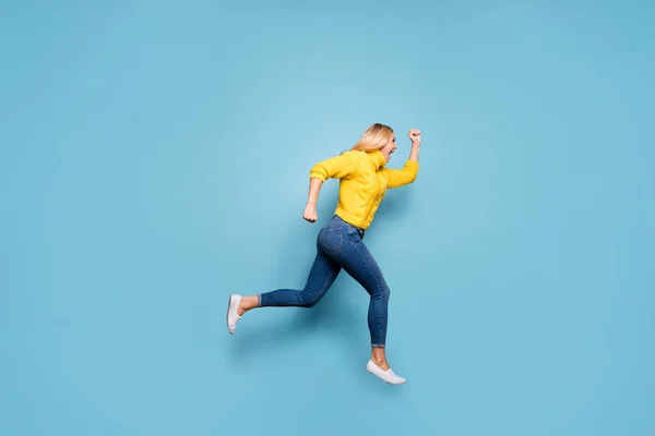 Foto de longitud completa de increíble señora rubia saltando alto corriendo descuento precios bajos ropa de compras de punto pantalones vaqueros de jersey amarillo aislado fondo de color azul — Foto de Stock