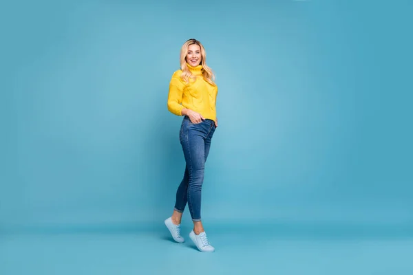 In voller Länge Foto von erstaunlichen blonden Dame schlank perfekte Formen Straße Herbst Look halten Hände in Taschen tragen gestrickte gelbe Pullover Jeans isoliert blaue Farbe Hintergrund — Stockfoto