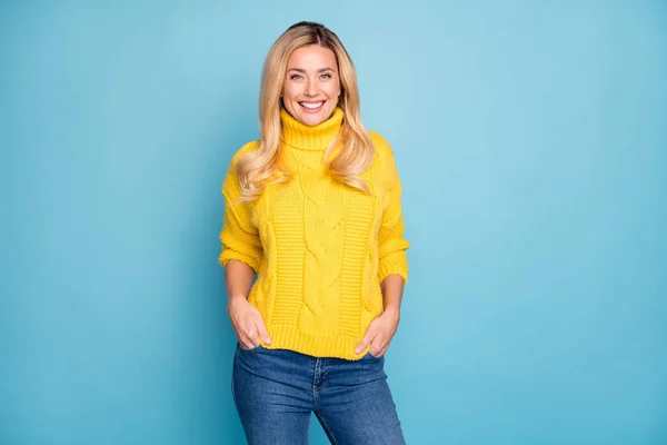 Fénykép elképesztő szép szőke hölgy fogas mosolygós jó hangulat fogja a kezét a zsebében viselni meleg kötött sárga jumper farmer elszigetelt kék háttér — Stock Fotó