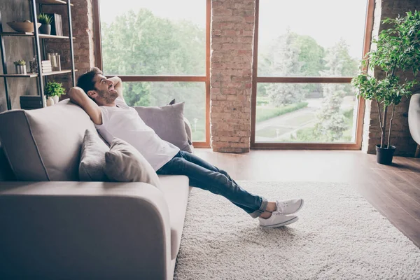 Perfil foto do cara de raça mista sentado sofá acolhedor de mãos atrás da cabeça relaxante ambiente de fim de semana acolhedor olhando sonhador novo desgaste de reparação roupa casual apartamento loft sala de estar dentro de casa — Fotografia de Stock