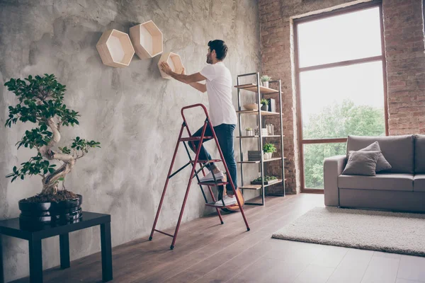 Full size profile view photo of mixed race guy installation wall shelf standing stepladder repair of new flat handmade working hanging last shelf checking sustainability flat indoors — Stock fotografie