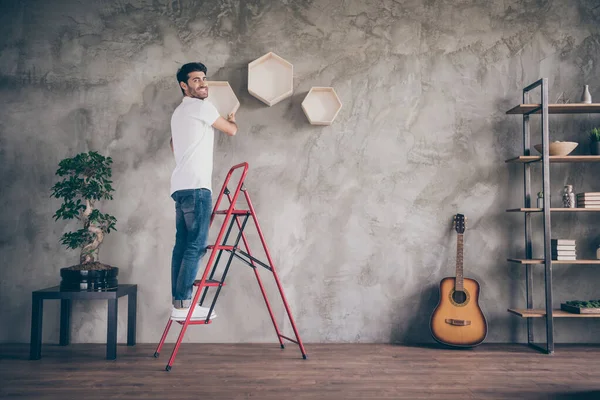 Full length profile view photo of mixed race guy installing wall shelf standing stepladder repair of new flat handmade working with pleasure hanging last shelf showing result indoors — Stock fotografie
