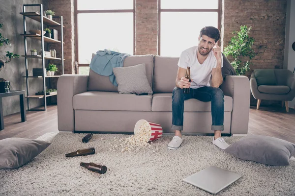 Zdjęcie mieszane wyścigu facet siedzi sofa trzymając butelki piwa popcorn na podłodze miał szalony rozrywki po imprezie cierpieć kaca rano ból głowy bałagan mieszkanie w pomieszczeniach — Zdjęcie stockowe
