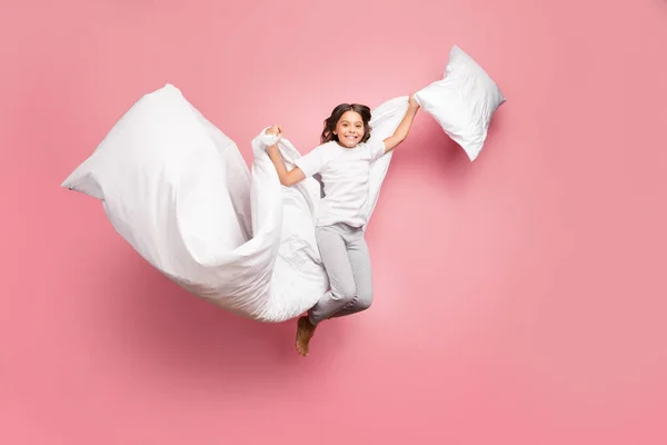 Full length body size view of nice attractive cute playful cheerful wavy-haired pre-teen girl jumping flying with soft cotton pillow blanket isolated over pink pastel color background — стоковое фото