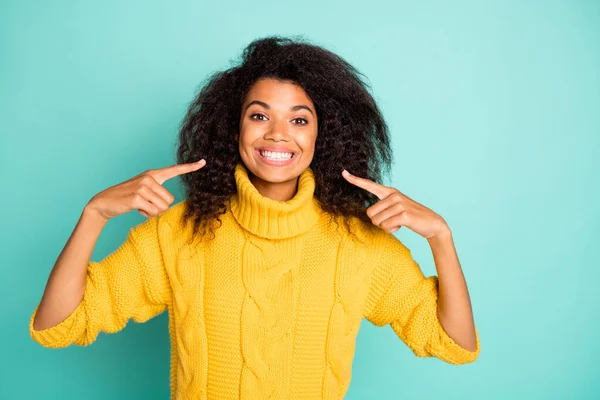 Photo of amazing dark skin curly lady indicating fingers on perfect condition teeth advertising dentist wear yellow knitted pullover isolated blue teal color background — Stockfoto