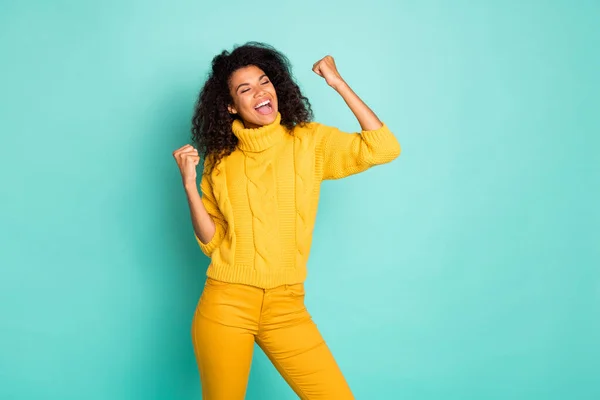 Photo of amazing dark skin lady holding hands raised celebrating lottery winning wear yellow knitted pullover stylish pants isolated blue teal color background — Stockfoto