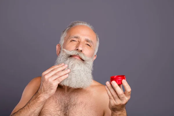 Foto di vecchio uomo maturo che applica gel sulla barba soddisfatto del suo effetto isolato sfondo di colore grigio — Foto Stock