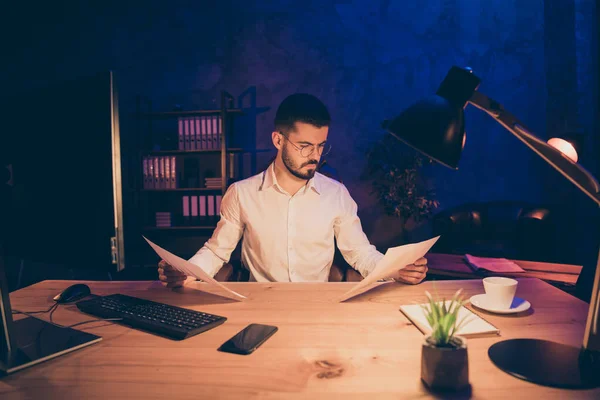 Retrato de foco startup trabalhador representante sentar tabela olhar ler documentos que ele precisa especialista analisar estatísticas para a sua empresa desenvolvimento estadia durante a noite no escritório loft escuro — Fotografia de Stock