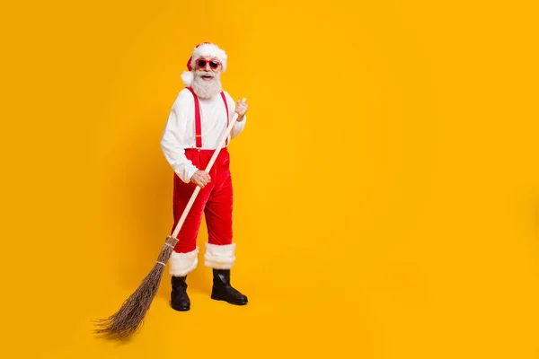 Foto de tamaño completo de Funky divertido barbudo abuelo trabajador en sombrero de Santa Claus disfrutar de x-mas tiempo Navidad Noel toallita escoba desgaste pantalones botas negras aisladas sobre brillo color fondo — Foto de Stock