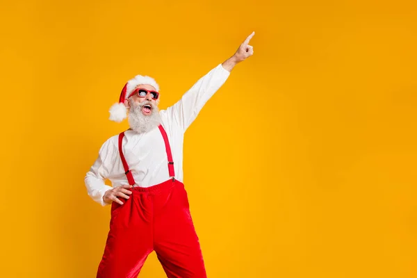 Retrato de engraçado louco santa claus hipster em chapéu vermelho diversão natal x-mas festa comemorar o novo ano dança levantar indicador dedo desgaste camisa suspensórios isolado amarelo cor fundo — Fotografia de Stock