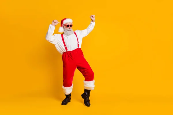 Teljes hosszúságú fotó a szürke haj hűvös vicces mikulás claus piros x-mas kalap élvezze újév karácsonyi mágia hagyomány ünneplés tánc ruha nadrágtartó csizma elszigetelt sárga háttér — Stock Fotó