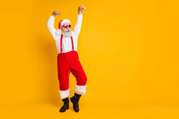 Foto de longitud completa de Santa Claus divertido loco en la danza de sombrero de hadas rojo levantar las manos celebración de la tradición de Navidad x-mas usar botas negras tirantes camisa aislado color amarillo fondo — Foto de Stock