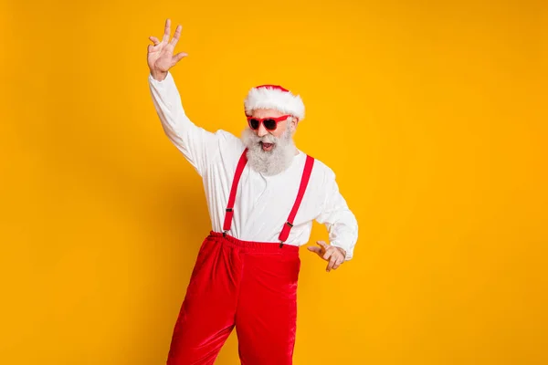 Retrato de positivo divertido santa claus hipster en sombrero rojo disfrutar de fiesta de Navidad evento divertido celebración de año nuevo club de baile desgaste tirantes de la camisa aislados sobre fondo de color amarillo — Foto de Stock