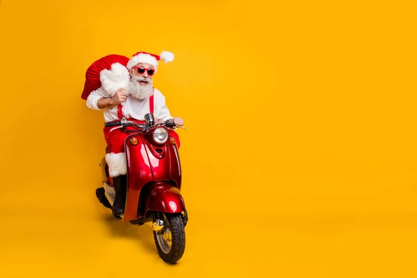 Full body foto van gekke grappige kerstman in rode hoed rijden snel motor fiets hold zak kerst x-mas voorbereiding rit noordpool dragen shirt bretels geïsoleerde gele kleur achtergrond — Stockfoto