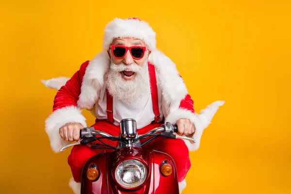 Rápida viagem de Natal. Louco hipster funky cabelos grisalhos santa claus em vermelho chapéu drive scooter pressa gritar desgaste camisa suspensórios isolados sobre fundo de cor brilhante — Fotografia de Stock