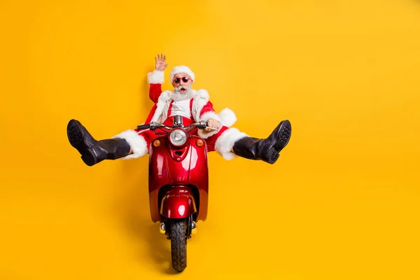 Full size foto van verraste gekke kerstman hipster in rode hoed shirt bretels rijden snelle motorfiets haast van noordpool vieren x-mas kerst feest geïsoleerde gele kleur achtergrond — Stockfoto