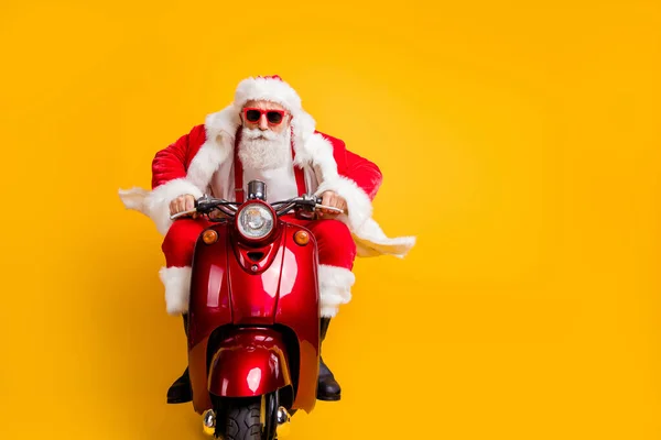 Retrato de graves hipster Papai Noel em chapéu vermelho unidade seu passeio piloto de scooter pressa para x-mas Natal partido desgaste camisa suspensórios isolados sobre fundo de cor amarela — Fotografia de Stock