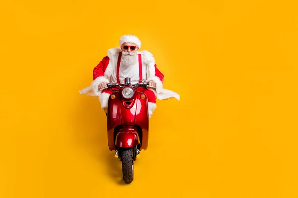 Full size foto van ernstige moderne santa claus hipster in rode pet hoed rijden scooter wil haast x-mas Nieuwjaar feest te dragen shirt bretels reizen geïsoleerde gele kleur achtergrond — Stockfoto