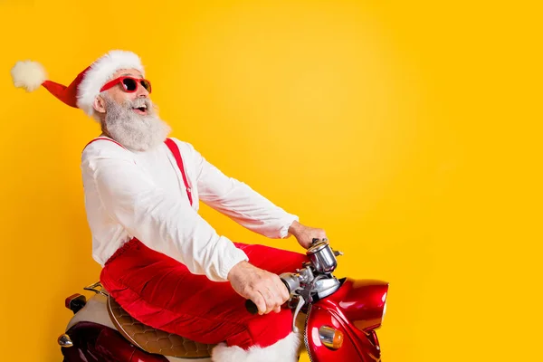 Profiel foto van stijlvolle santa wit haar opa haasten x-mas themafeest door retro fiets dragen trendy zon specs rode broek cap shirt geïsoleerde gele kleur achtergrond — Stockfoto