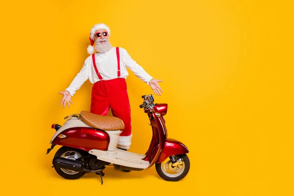 Foto de cuerpo completo de santa man listo para la fiesta temática de x-mas de pie cerca de la bicicleta que presenta el traje fresco desgaste de moda sol especificaciones pantalones gorra camisa aislado color amarillo fondo —  Fotos de Stock