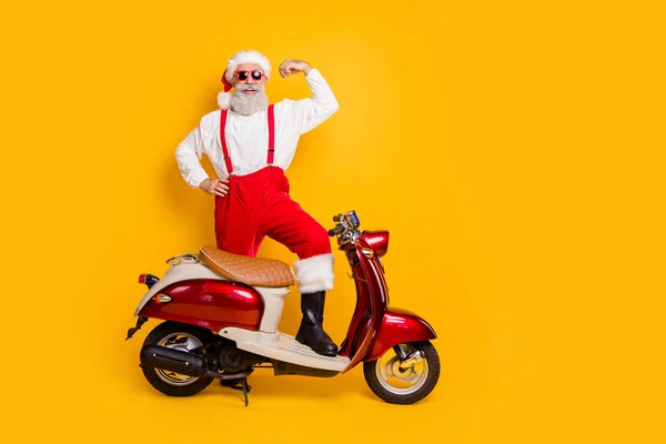 Full body photo of santa ambicioso homem stand near moped show força bíceps entregue pesados presentes desgaste moderno sol especificações calças cap shirt isolado amarelo cor fundo — Fotografia de Stock