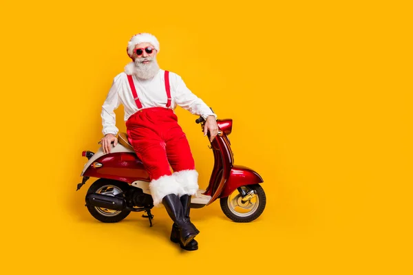 Full body foto van de kerstman klaar voor x-mas thema partij zitten retro fiets oprecht glimlachen dragen trendy zon specs broek cap shirt laarzen geïsoleerde gele kleur achtergrond — Stockfoto