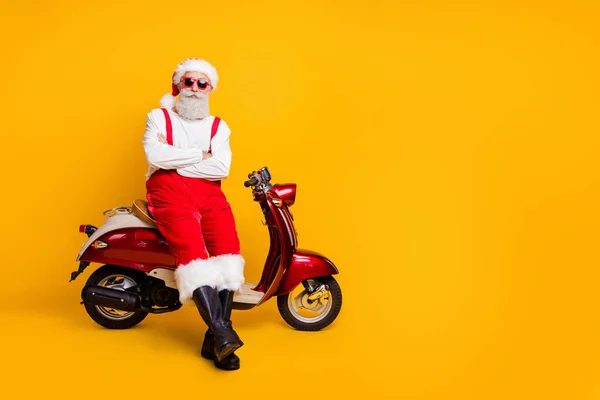 Foto de corpo inteiro de auto-confiante Papai Noel humor festivo pronto x-mas tema partido sentado bicicleta retro desgaste sol especificações calças boné botas isoladas cor amarela fundo — Fotografia de Stock