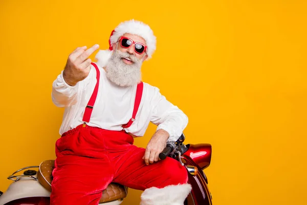 Zdjęcie szalone siwe włosy Mikołaj siedzi na rowerze pokazując niegrzeczny gest niedbały nastrój zła osoba nosić okulary okulary spodnie czapka koszula odizolowany żółty kolor tło — Zdjęcie stockowe