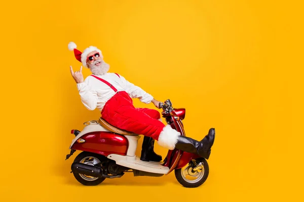 Pełne ciało zdjęcie śmieszne białe włosy Mikołaj w świąteczny nastrój jazda x-mas motyw party na rowerze pokazując rogi nosić okulary okulary spodnie czapka buty odizolowany żółty kolor tło — Zdjęcie stockowe