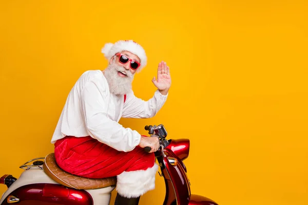 Photo of stylish Santa dziadek jazda X-mas party retro rower machanie ramię powitanie gest nosić modne okulary czerwone spodnie czapka koszulka buty odizolowany żółty kolor tło — Zdjęcie stockowe
