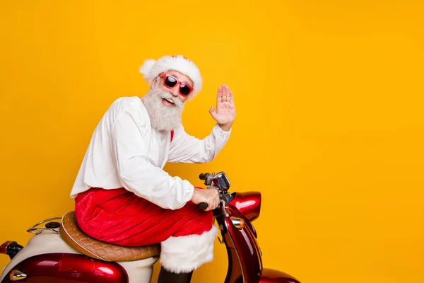 Foto do elegante santa vovô equitação x-mas festa retro bicicleta acenando braço saudação gesto desgaste moda sol especificações vermelho calças boné camisa botas isolado amarelo cor fundo — Fotografia de Stock