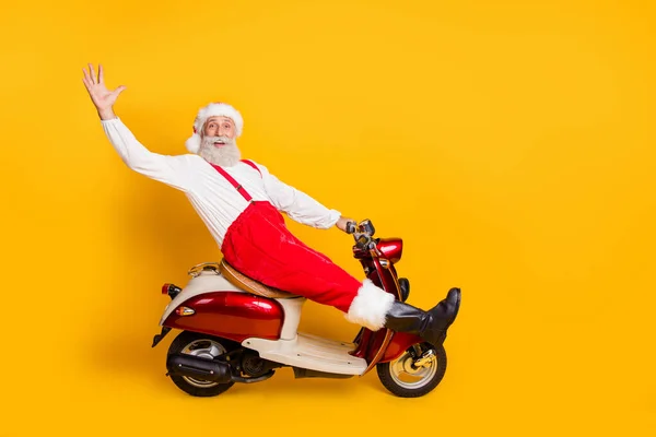 Foto de comprimento total de engraçado santa branco cabelo avô apressando newyear x-mas festa tema por bicicleta dizendo Olá desgaste calças cap suspensórios botas isoladas cor amarela fundo — Fotografia de Stock