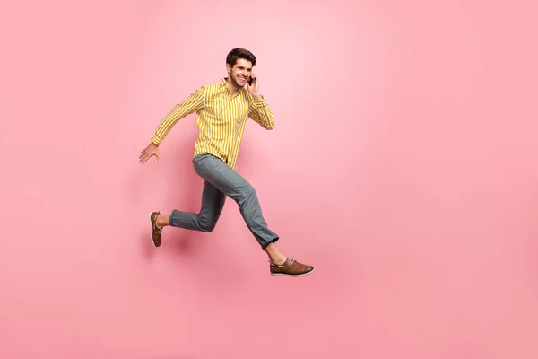 Profilo completo del corpo foto di bel ragazzo salto alto tenere telefono parlando con fidanzata data affrettata indossare pantaloni camicia a righe isolato colore rosa sfondo — Foto Stock